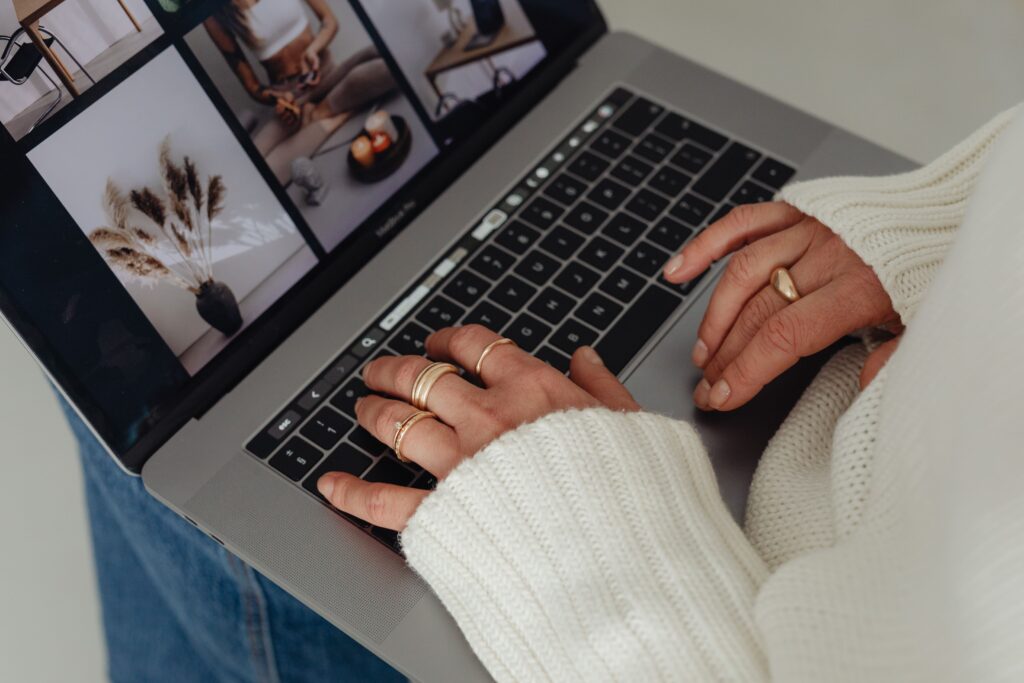 Person browsing stock photography on a laptop for a wellness website, selecting calming visuals like flat lays, natural light, and minimalist interiors for brand design.