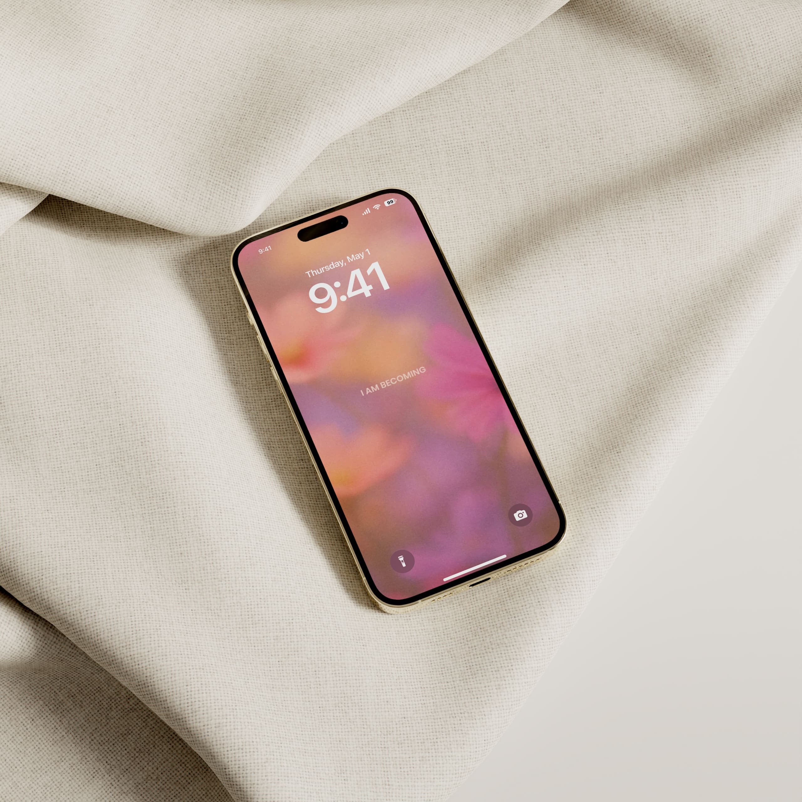 iPhone placed on soft beige fabric showing a blurred floral wallpaper with the text “I AM BECOMING” on screen.