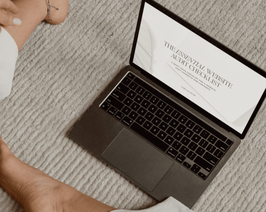 Woman sitting on a cozy rug with a laptop displaying ‘The Essential Website Audit Checklist.