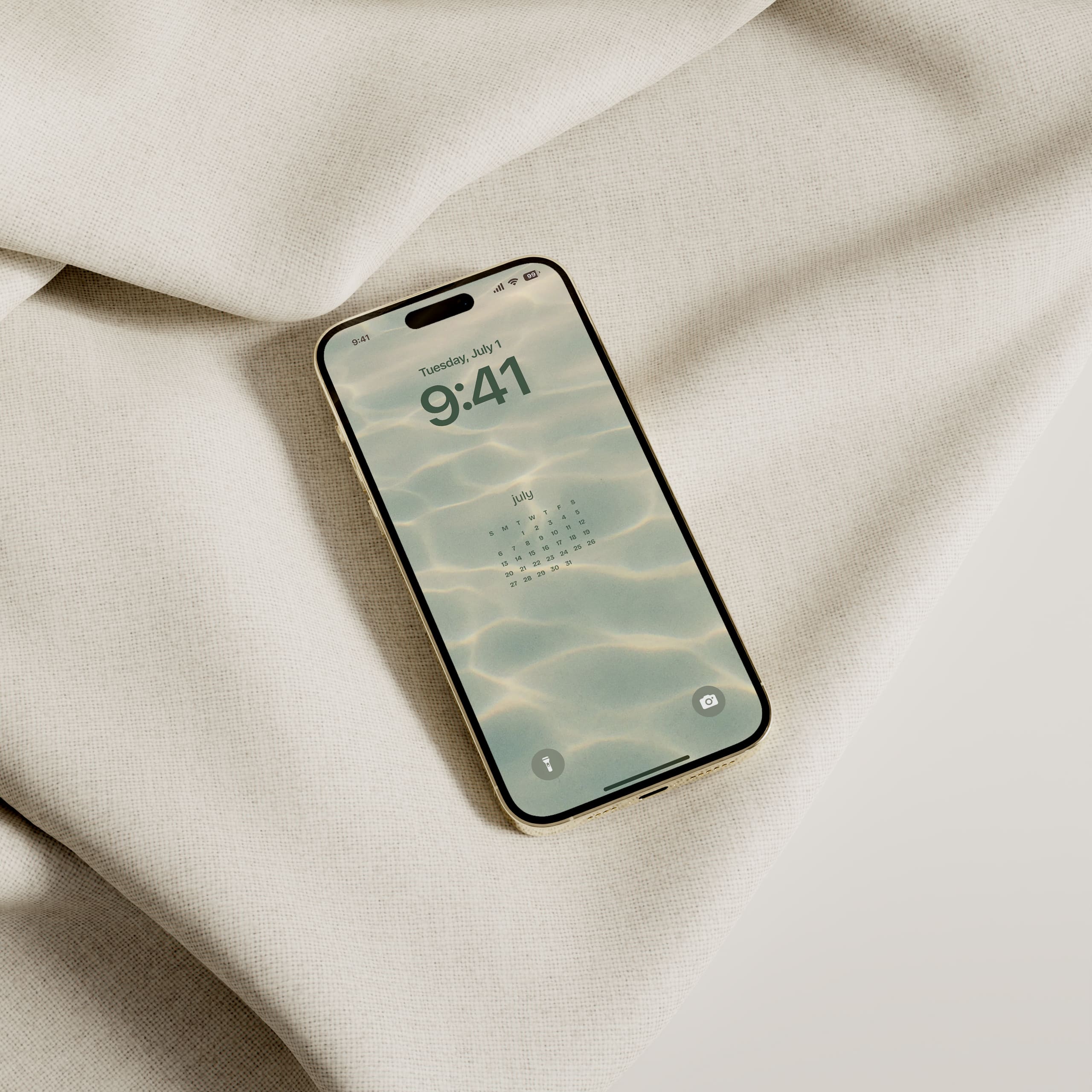 iPhone displaying July 2025 calendar wallpaper with a soft water background, resting on neutral fabric.
