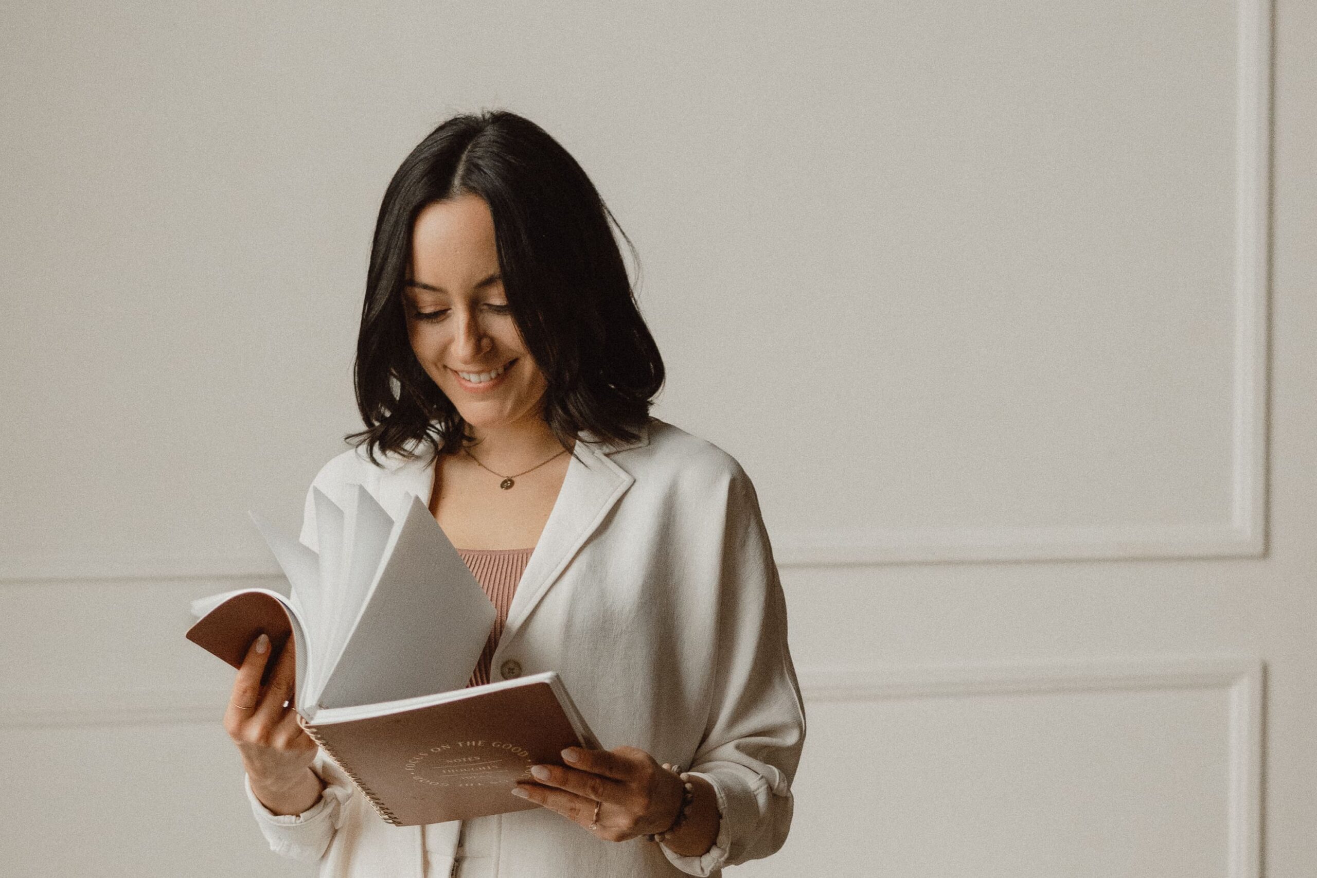 Smiling woman flipping through a journal in a neutral studio setting — representing wellness professionals organizing their legal pages.
