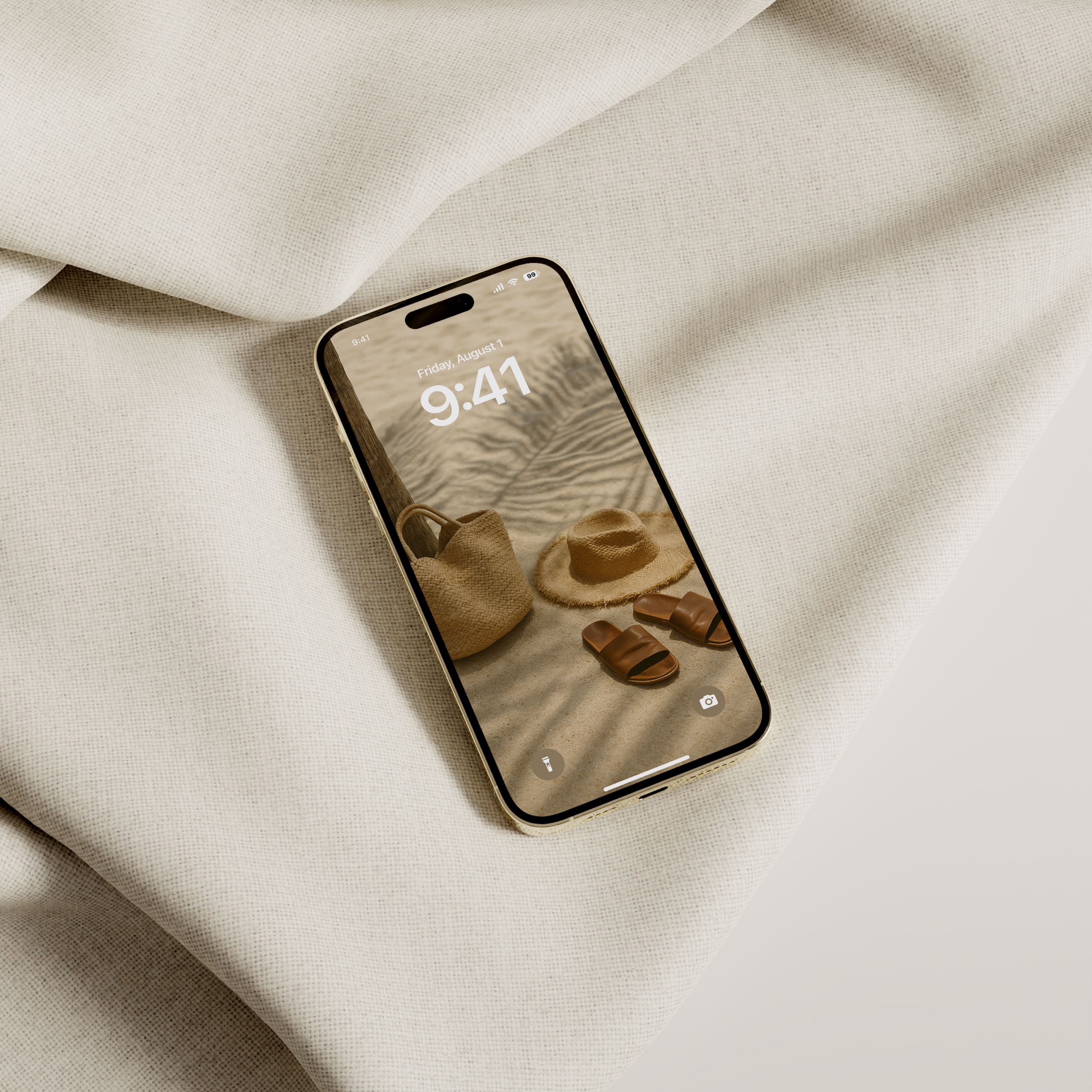 iPhone with August wallpaper featuring a beach tote, hat, and sandals resting in palm tree shade, styled on a neutral fabric background.