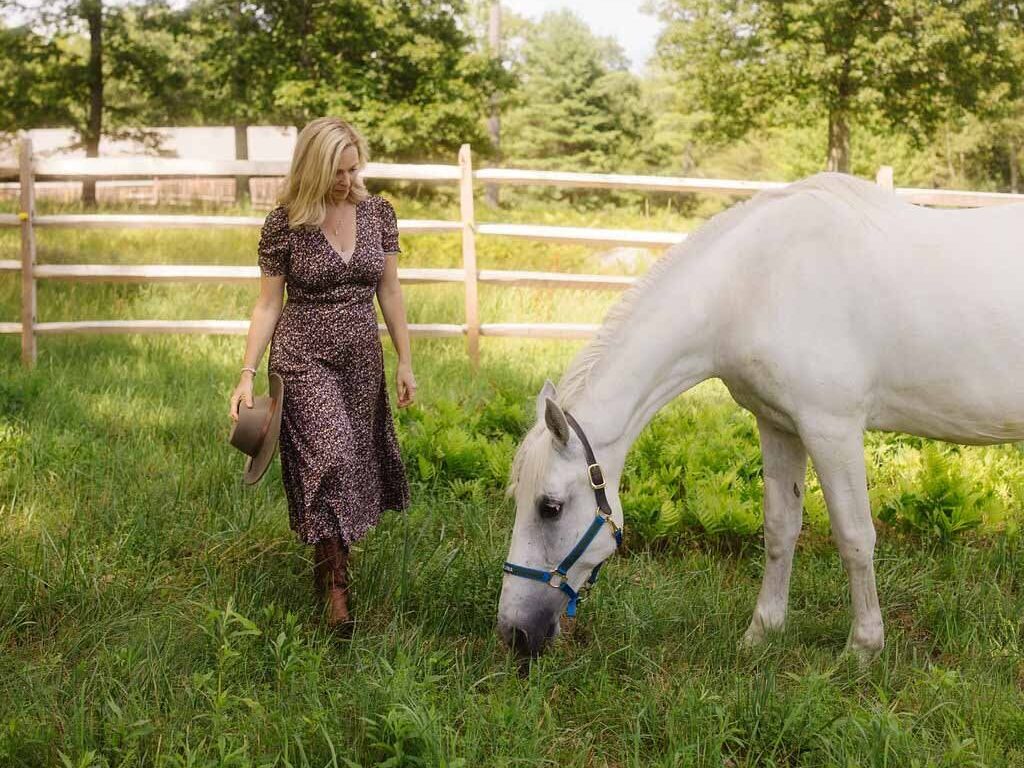 Leiko, founder of Peace Horse Collective, walking with her white horse in a quiet pasture during an equine-assisted learning session in the Berkshires.